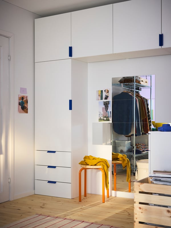PLATSA storage system in white, with one wardrobe and a line of cabinets up along the ceiling, mirrors on the wall below.