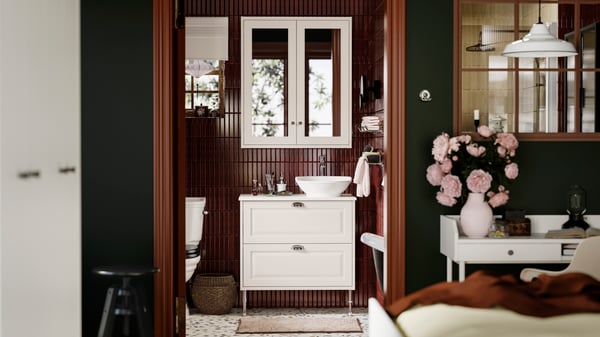 A contemporary bathroom with terrazzo floors, featuring a TÄNNFORSEN wash-stand and a dark maroon tile wall.