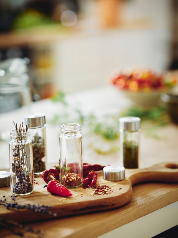 Dried spices and herbs in glass/stainless steel ÖRTFYLLD spice jars on an oak ARTISTISK chopping board.