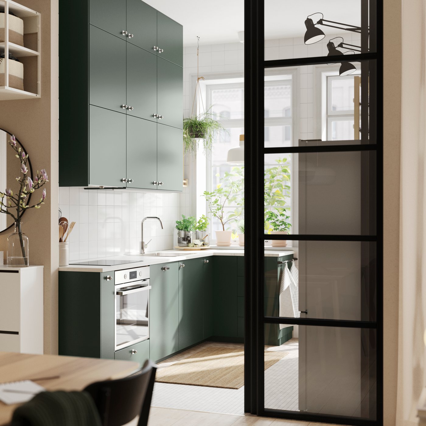 An open kitchen with deep green HAVSTORP kitchen fronts and wall cabinets up to the ceiling, next to a bright living room.