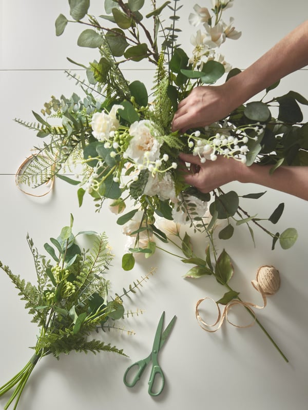 Green and white SMYCKA flowers and leaves being arranged into a bouquet.