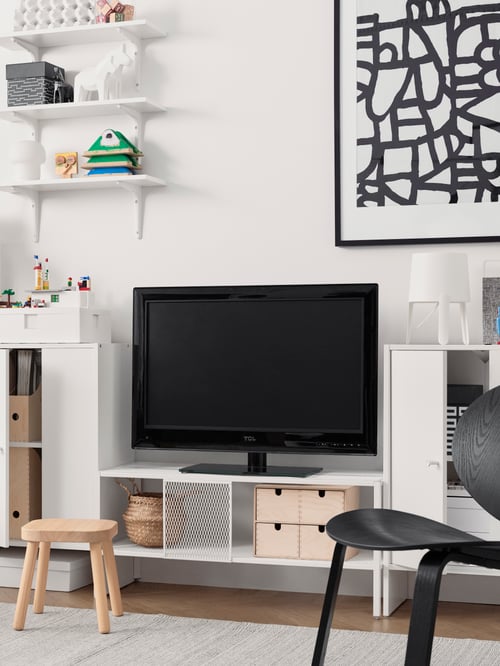 A white TV bench, a black TV, a framed black and white print, white cabinets with doors, decorative objects.