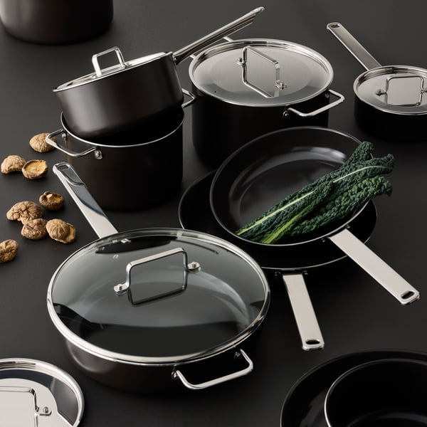 A close-up of a black-grey GULDÖRING sauté pan with lid is placed on a table with greens and nuts nearby.