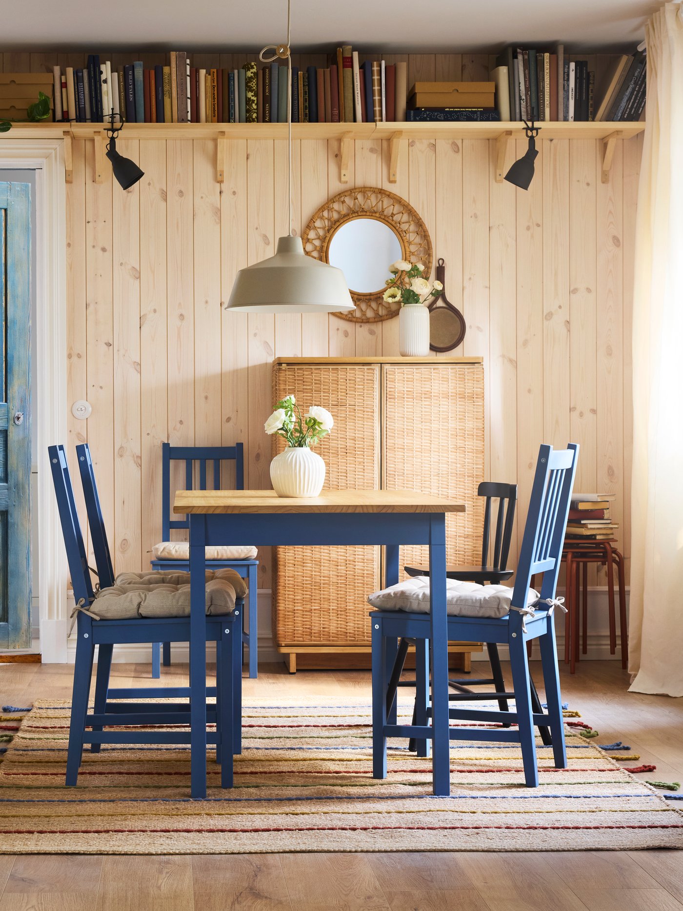 Blue stained/pine PINNTORP chairs stand at a PINNTORP table on top of a handwoven RAKLEV rug in a Scandinavian dining room.