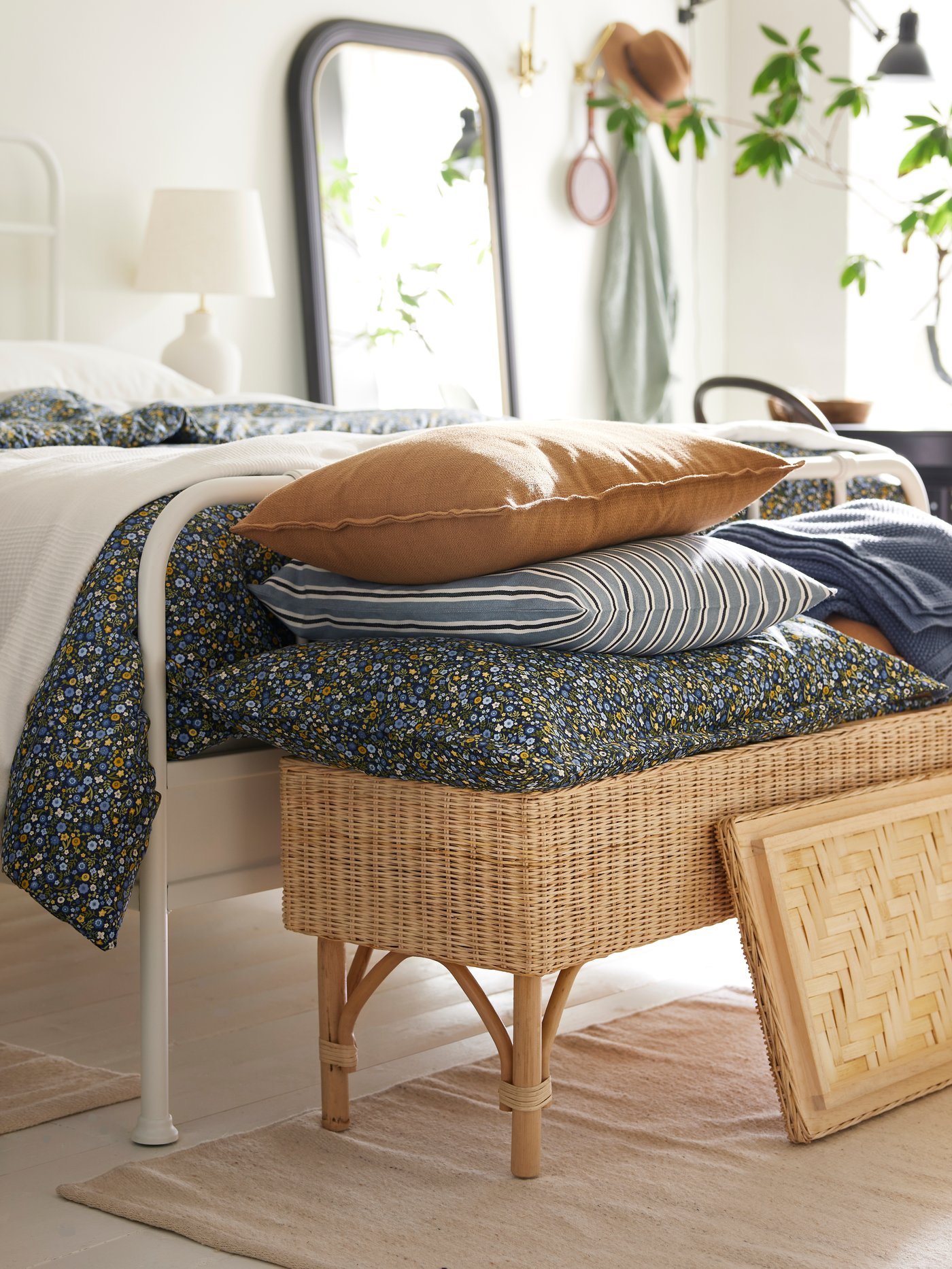 Een kussen met een ROSENTIBAST hoes en een sierkussen in een LAGERPOPPEL hoes, boven op een rattan TOLKNING bankje met opbergruimte.