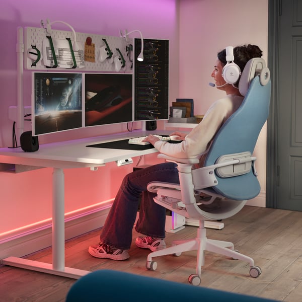 En person sitter i en BÄSTBOLL gamingstol vid ett vitt MÅLOMRÅDE gamingbord. Två NÄVLINGE spotlights är fästa på bordet.