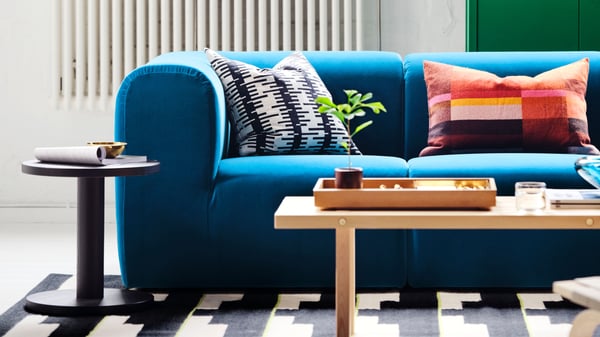 En närbild på en blå soffa med mönstrade kuddar, ett svart sidobord och ett ljust soffbord på en svartvit mönstrad matta.