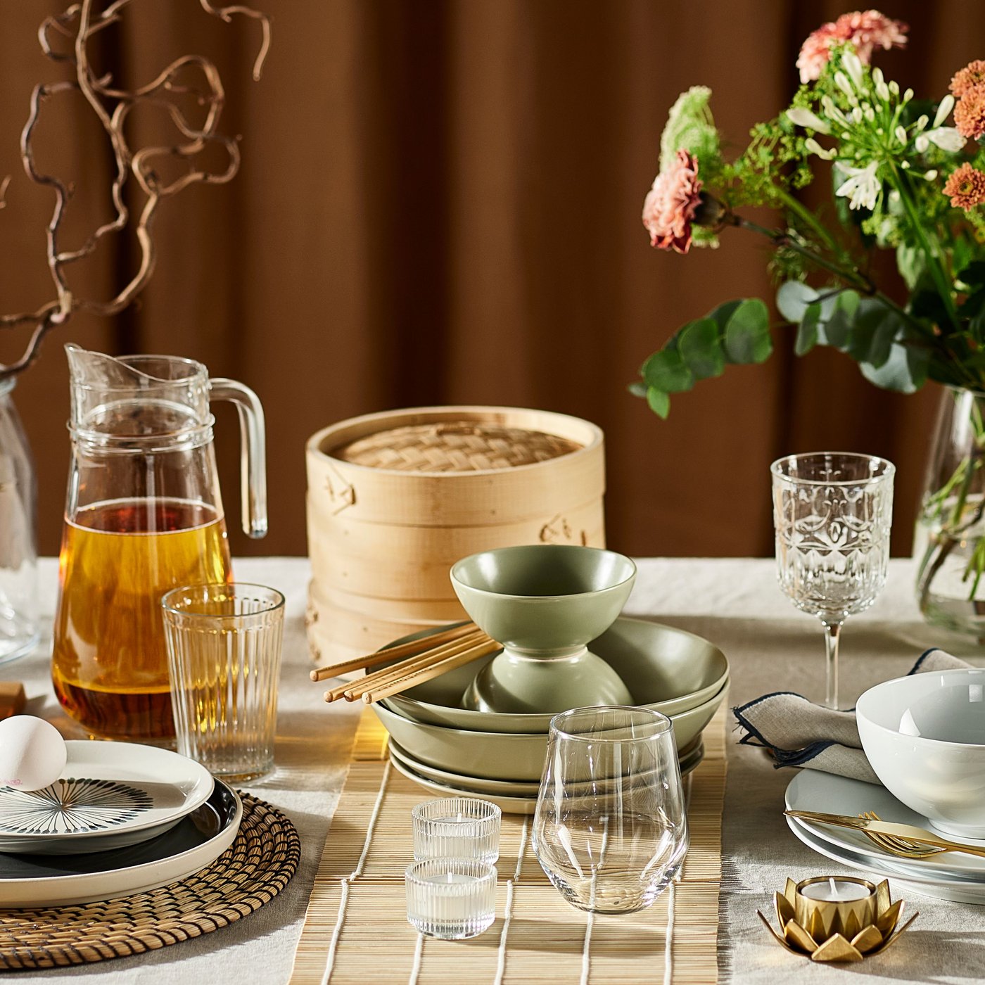 Part of a table with many items on it including flowers, glasses, matt green FÄRGKLAR dishes and a TILLBRINGARE jug.