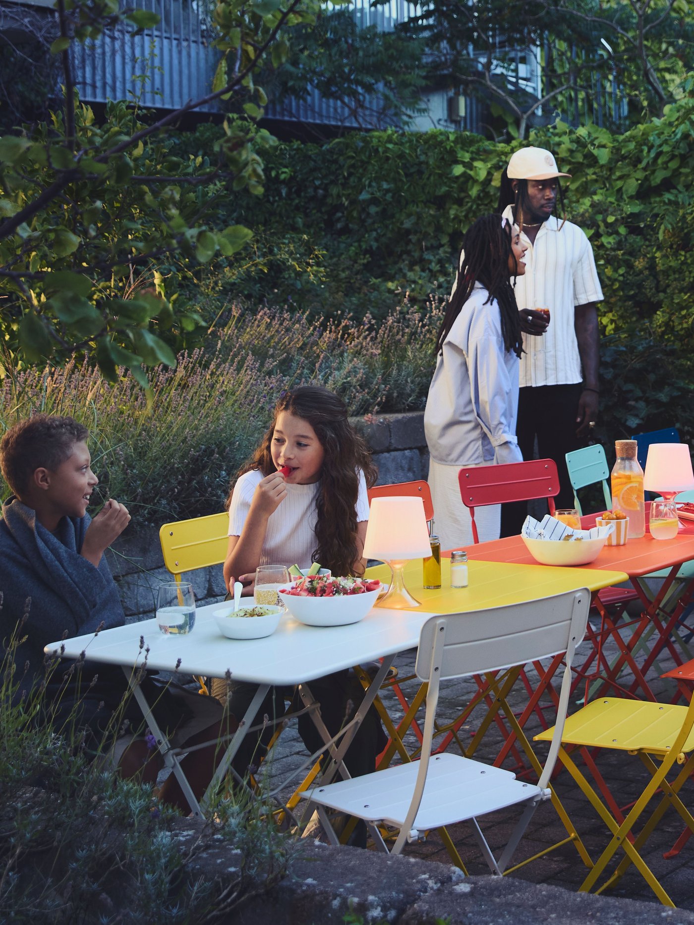 Les voisins se sont rassemblés dans la cour autour de tables SUNDSÖ colorées, disposées en une longue table rouge, bleue, jaune et blanche.