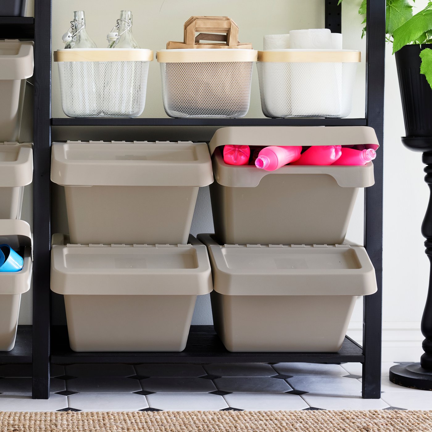 Fire SORTERA affaldssorteringsspande står på en sort IVAR reol den ene SORTRA affaldsspands låg står let åben og er fyldt med lyserøde plastik dunke på øverste hylde i reolen sår tre trådkurve. 