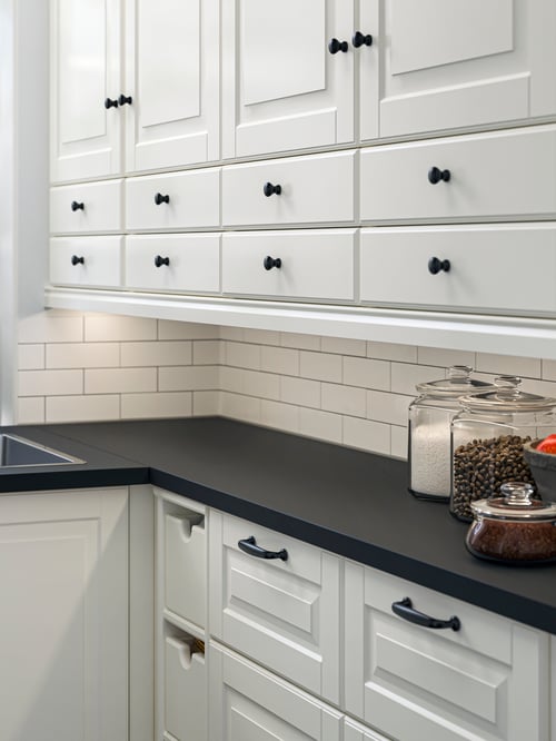 A kitchen with BODBYN fronts and cabinets in off-white. There are two plants sitting on a windowsill next to the sink.