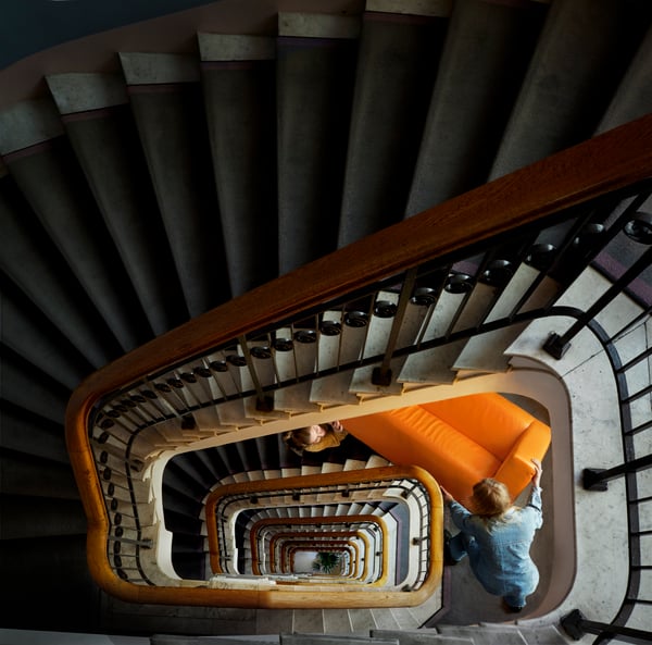 Two persons trying to carry a sofa on a curved staircase.