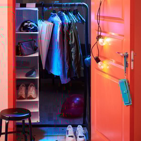 Neon-lit room with a white shelving unit, hanging garments, and an red balloon on the floor.
