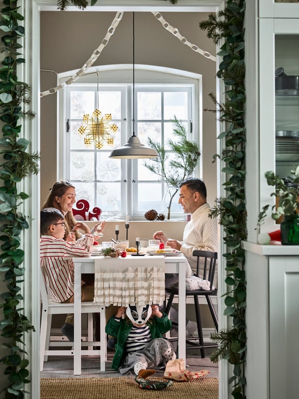 Family gathered around a traditional Scandinavian white HAUGA table and three HAUGA chairs in rustic Christmas dining setting.