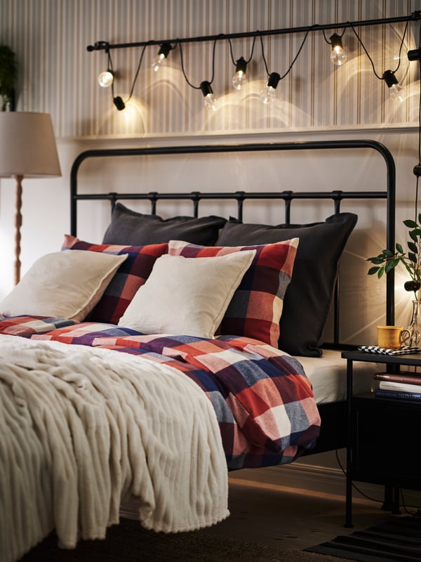 Bedroom with STJÄRNÖ bed frame and SVARTRÅ led lighting chain on the wall above. The bedding in warm red, blue and beige.