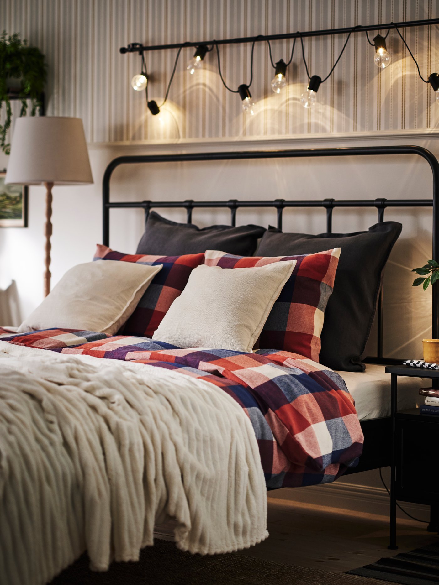 Bedroom with STJÄRNÖ bed frame and SVARTRÅ led lighting chain on the wall above. The bedding in warm red, blue and beige.
