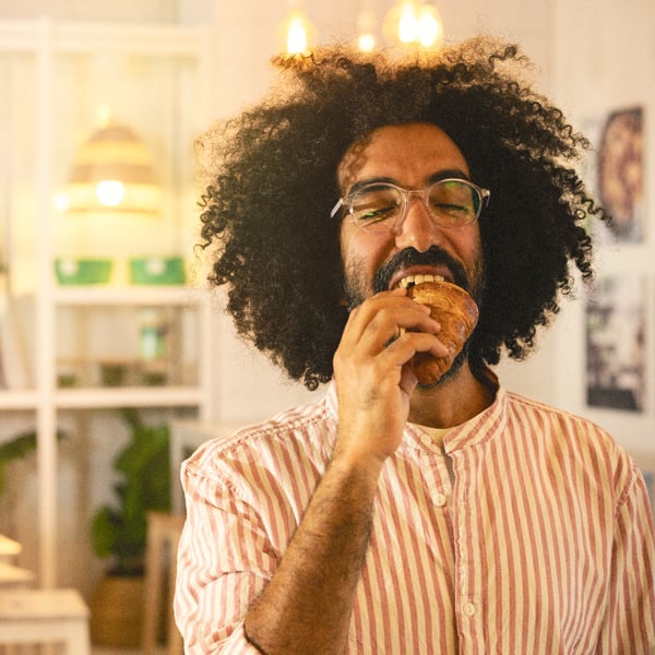 A person wearing a striped shirt takes a large bite of a breakfast croissant.