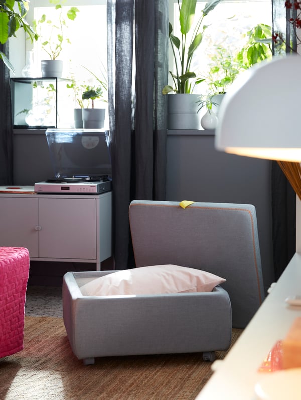 An IKEA SLÄKT light grey seat module, with castors and padded cushion, opened to reveal the storage space within.