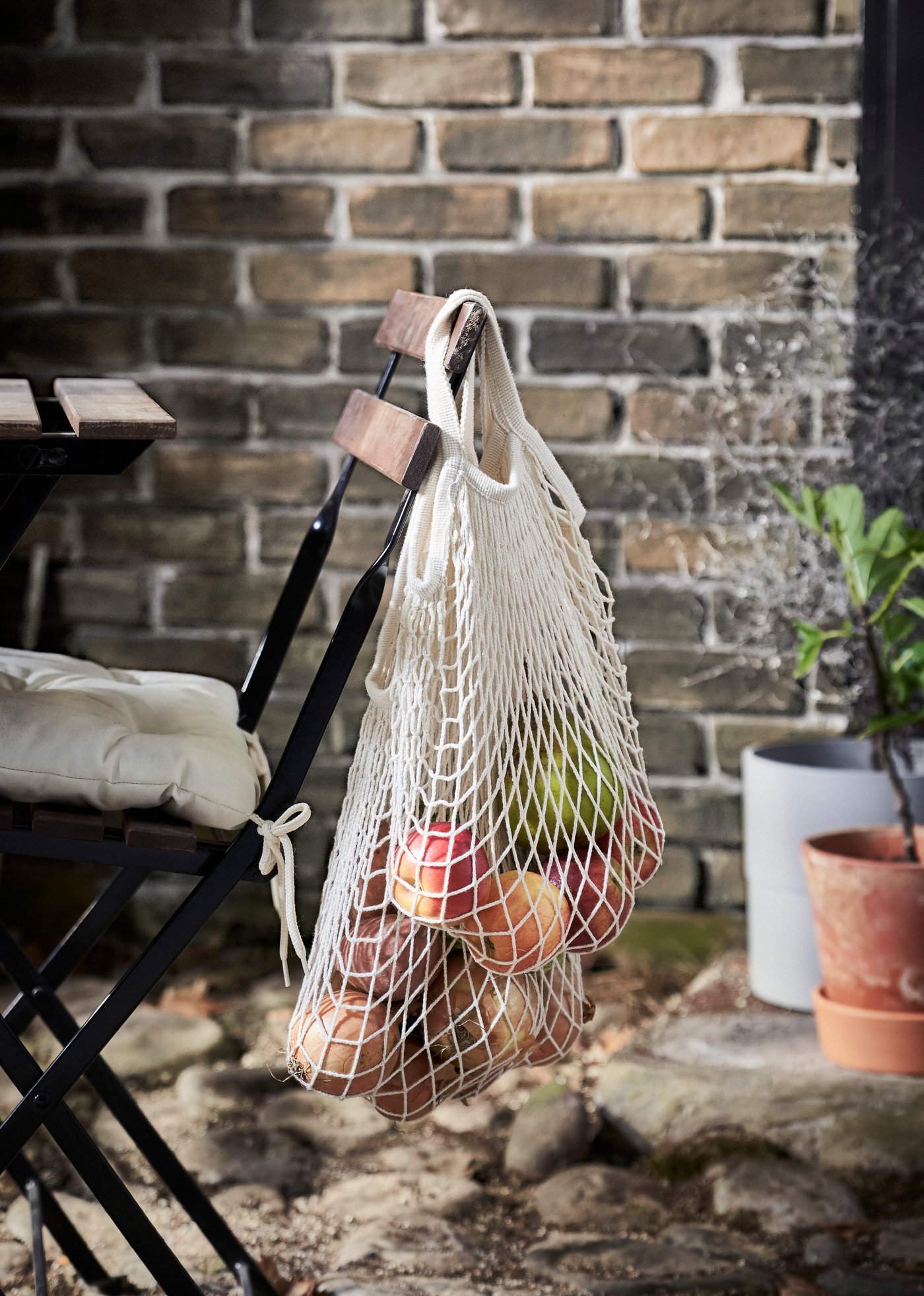 Una borsa a rete KUNGSFORS in materiale naturale appesa ad una sedia con all'interno degli alimenti.