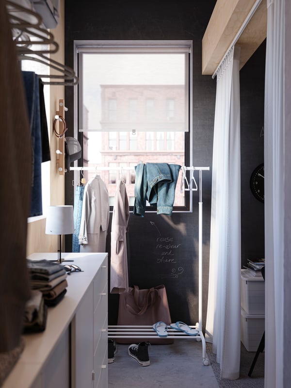 A white RIGGA clothes rack with items of clothing on hangers and folded over the top, behind a VIHALS storage combination.