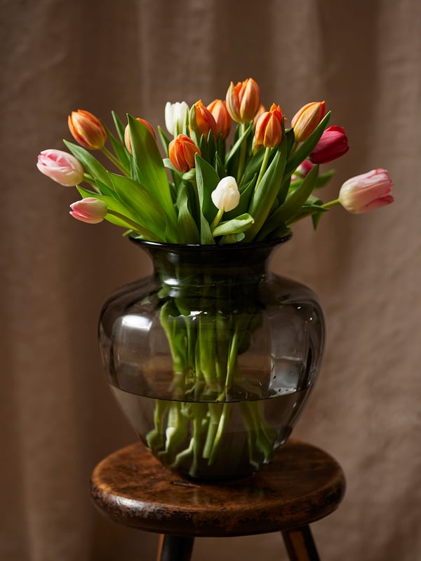A grey TONSÄTTA vase with an hourglass shape with a bunch of colourful tulips in it.