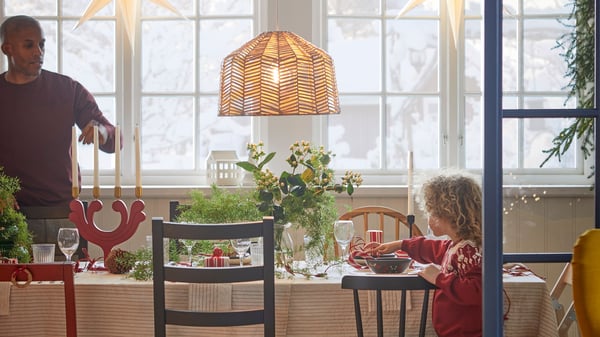 Festive dining setting with striped VIPPSTARR tablecloth, mix and match chairs and STRÅLA star pendant lampshade in window.