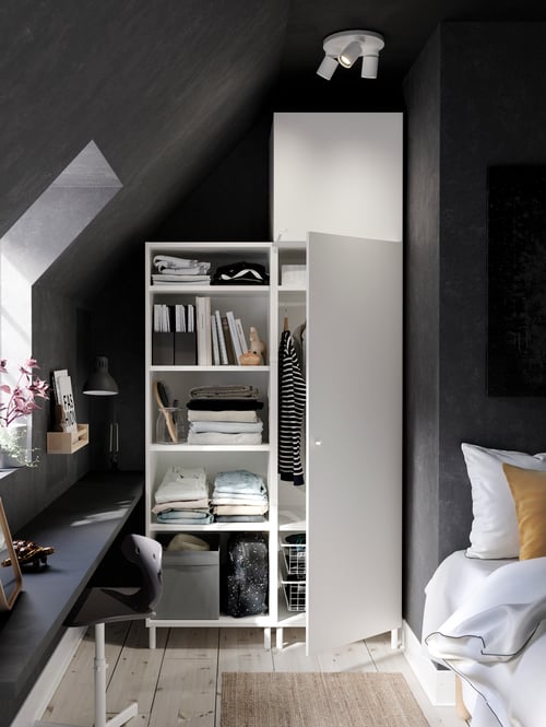 Ein Fonnes weißer PLATSA Kleiderschrank mit Regalen und zwei Schränken unter einem Schrägdach in einem Schlafzimmer. Eine Tür steht offen.
