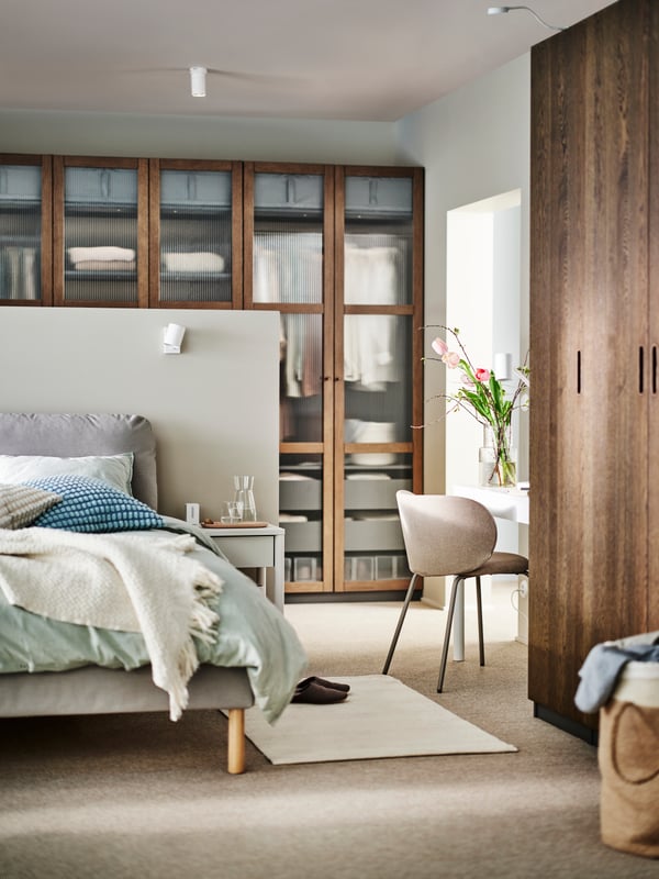 A Diseröd brown SAGESUND upholstered bed covered in green/stripe BERGPALM bed linen and a cushion in a SVARTPOPPEL cover.