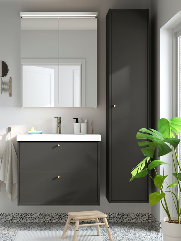 A dark grey HAVBÄCK wash-stand with two drawers has a tall HAVBÄCK cabinet next to it and a mirror cabinet with above it.