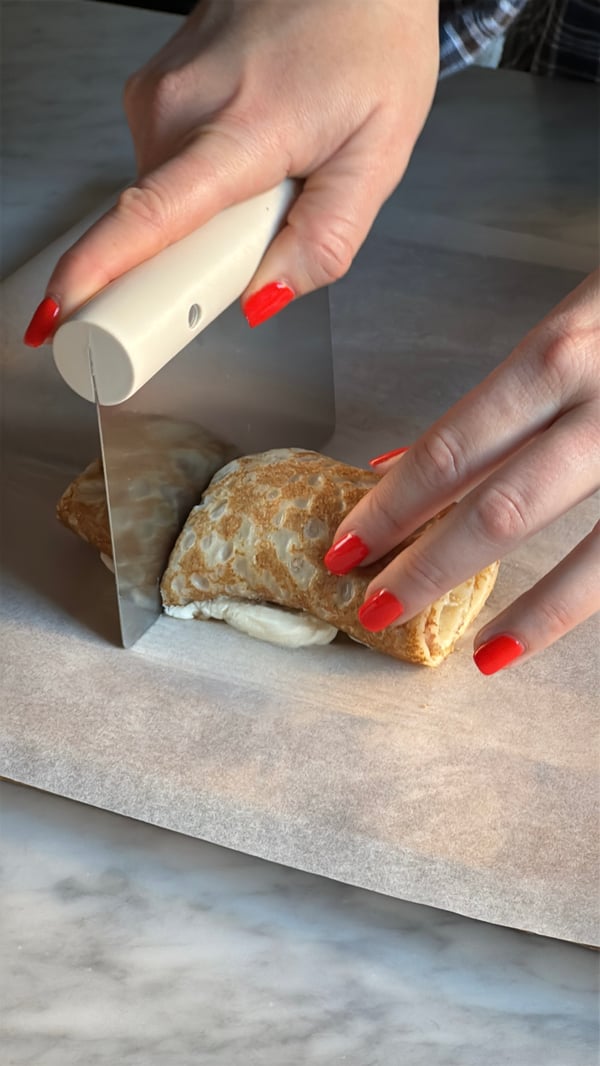 En person delar en ihoprullad pannkaka med en LÄTTBAKAD degskärare.