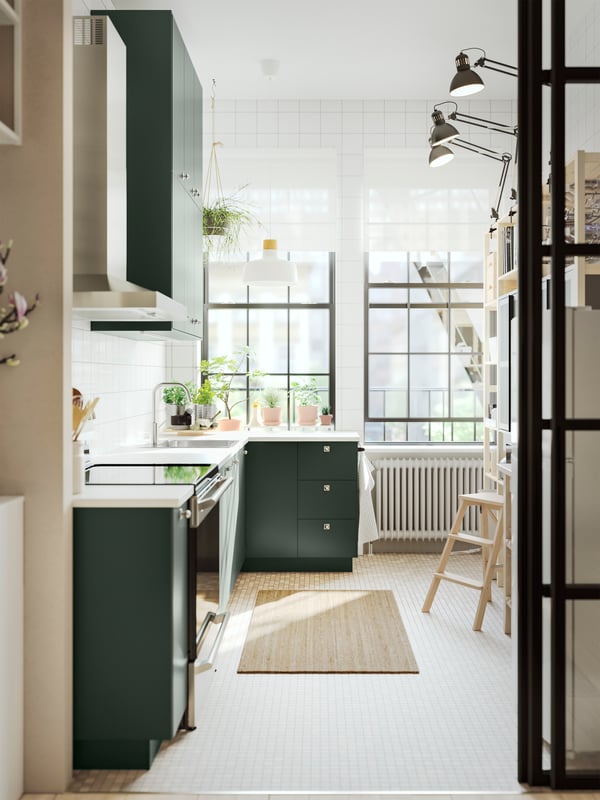 A kitchen with deep green kitchen fronts, a white marble effect/laminate EKBACKEN worktop and a white/birch pendant lamp.