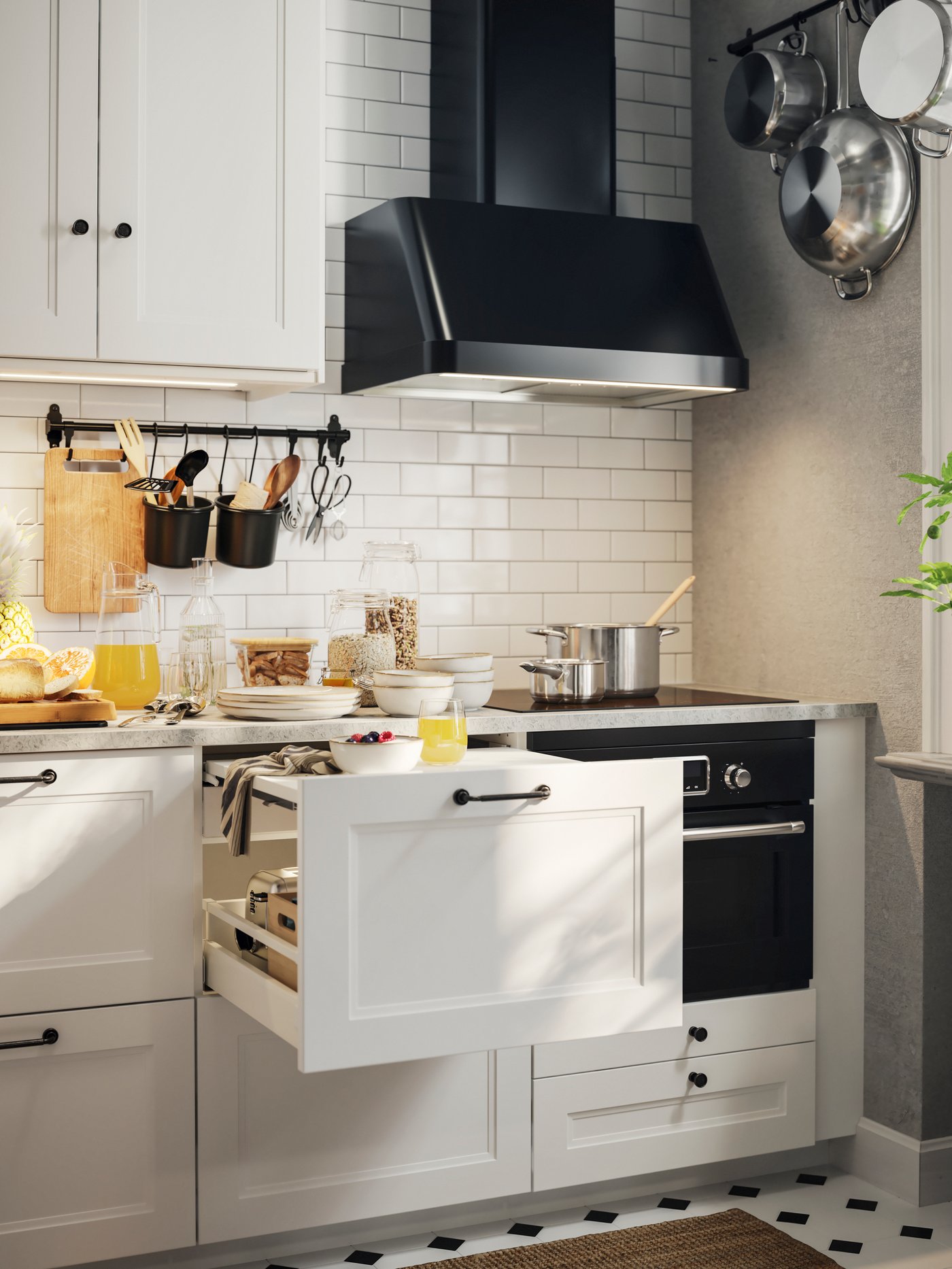A kitchen with matte white AXSTAD fronts. The top drawer in one cabinet has a pull-out shelf with a bowl and a glass on it.