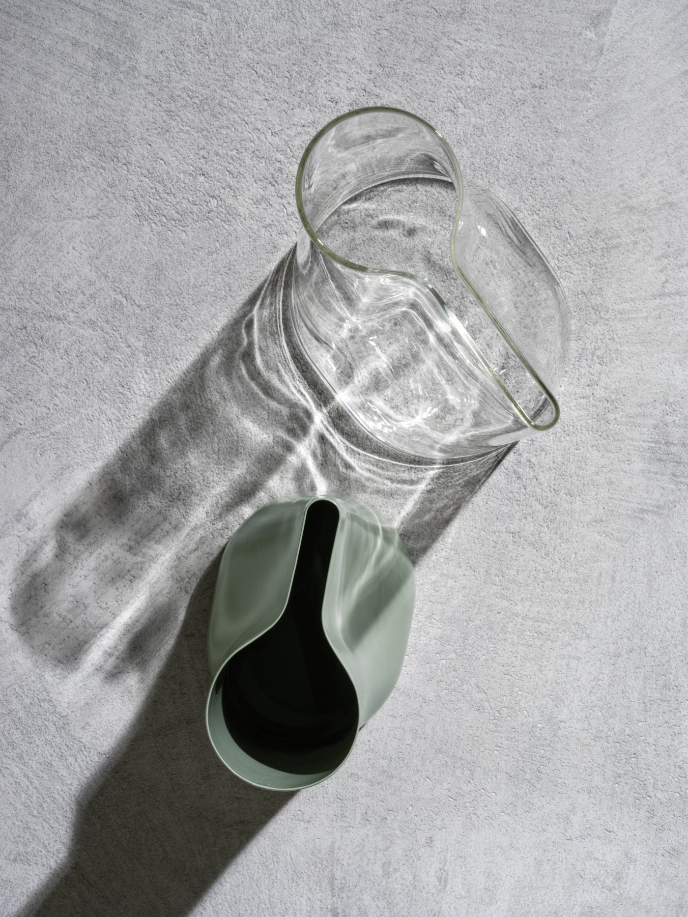 Dues regadores/gerros CHILIFRUKT de vidre transparent i verd acerat posades sobre una superfície de formigó gris.
