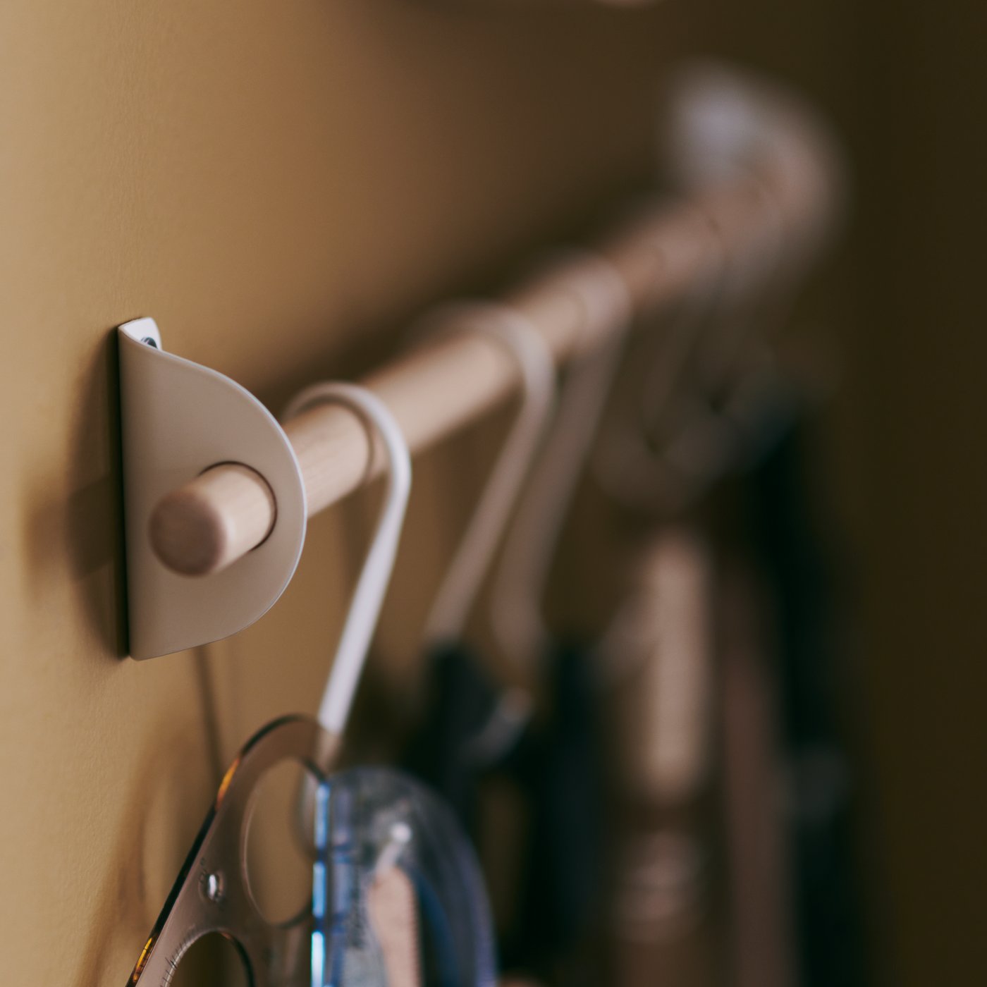 Close-up of the NEREBY rail, made of birch wood, with white NEREBY hooks hanging from it.