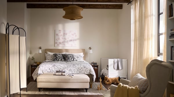Recámara en beige y blanco con una cama infantil junto a una cama de adultos y un sillón en primer plano.