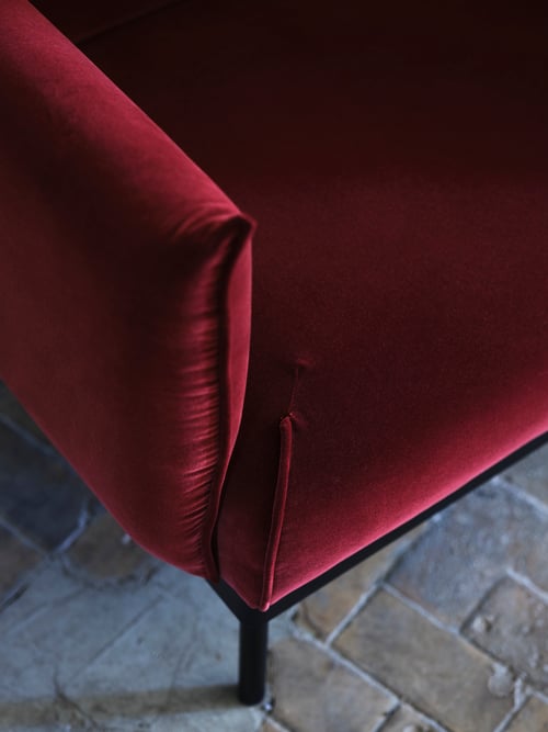 Living room with red-brown two-seat sofa, with high armrests and velvet-looking surface, placed on the floor with tiles.