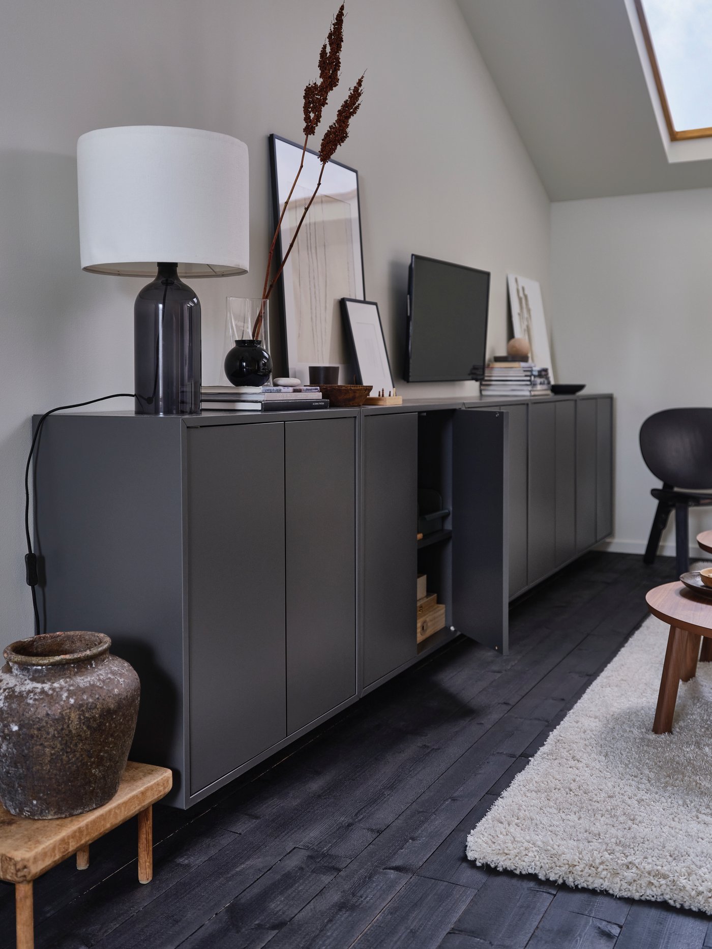 Na ścianie wisi kombinacja szafek EKET z przedmiotami z ceramiki i szkła oraz książkami i innymi osobistymi przedmiotami.