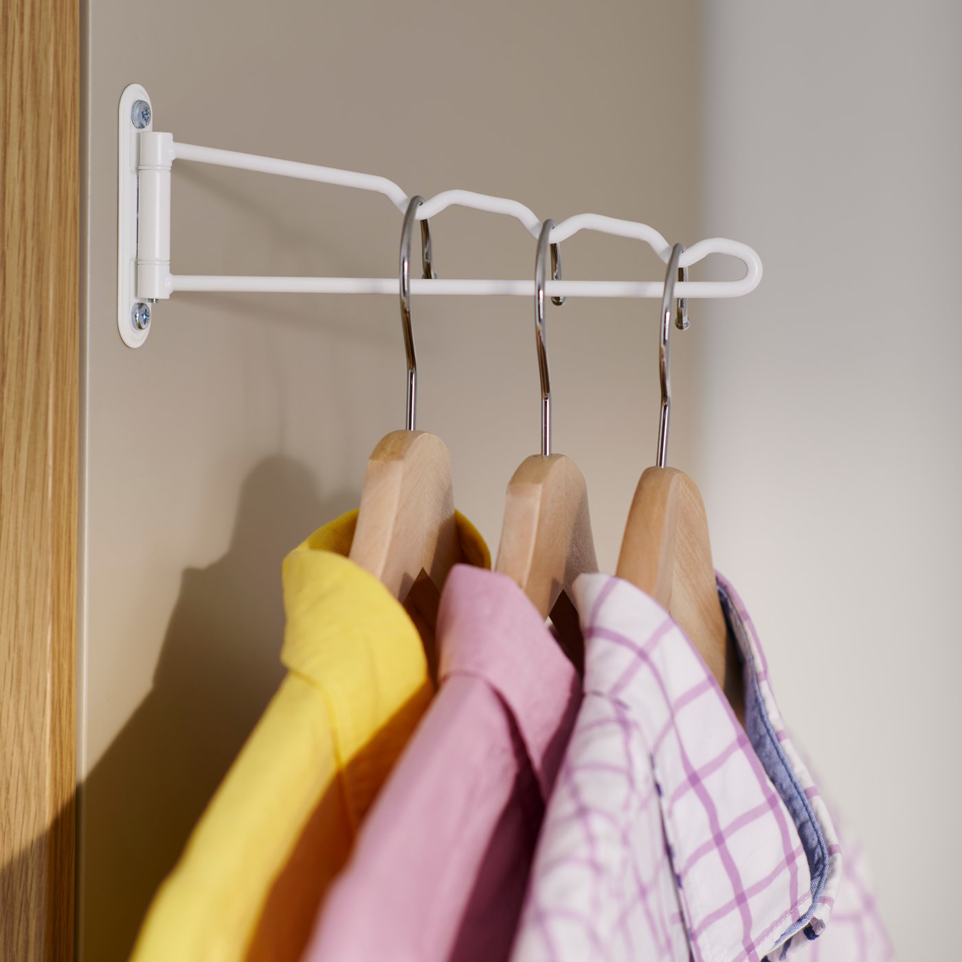 A close up of KOMPLEMENT valet hanger with three colourfull shirts on hangers hanging from it.