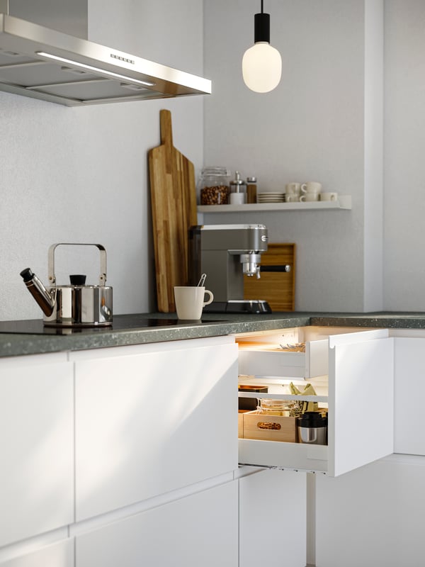 A kitchen corner in a kitchen with smooth white VOXTORP fronts. One top drawer is pulled out, showing things stored inside.