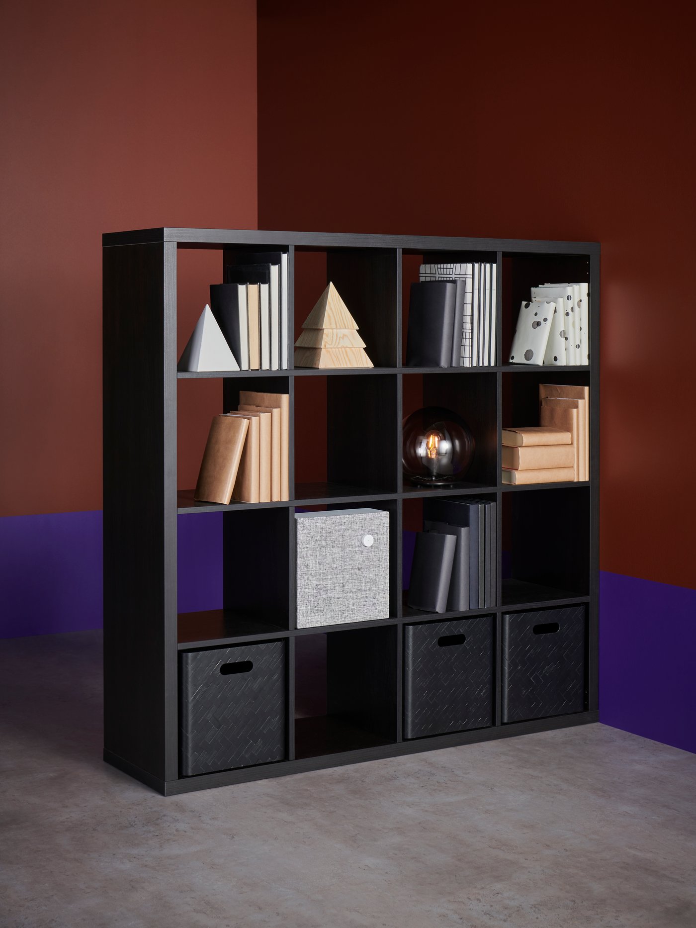 Espacio de trabajo con estantería, altavoz Bluetooth, cajas, lámpara de mesa, libros, agendas, sobres de papel y objetos personales.