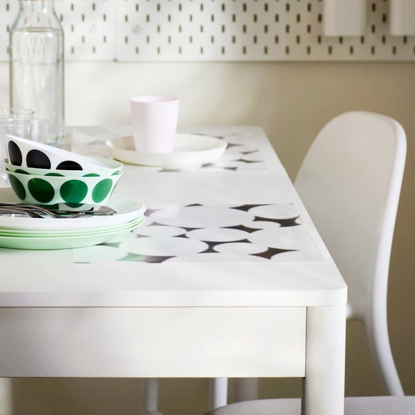 A TONSTAD extendable table in white in a room with bowls, plate and a beaker on it, and an ANTILOP highchair in white.