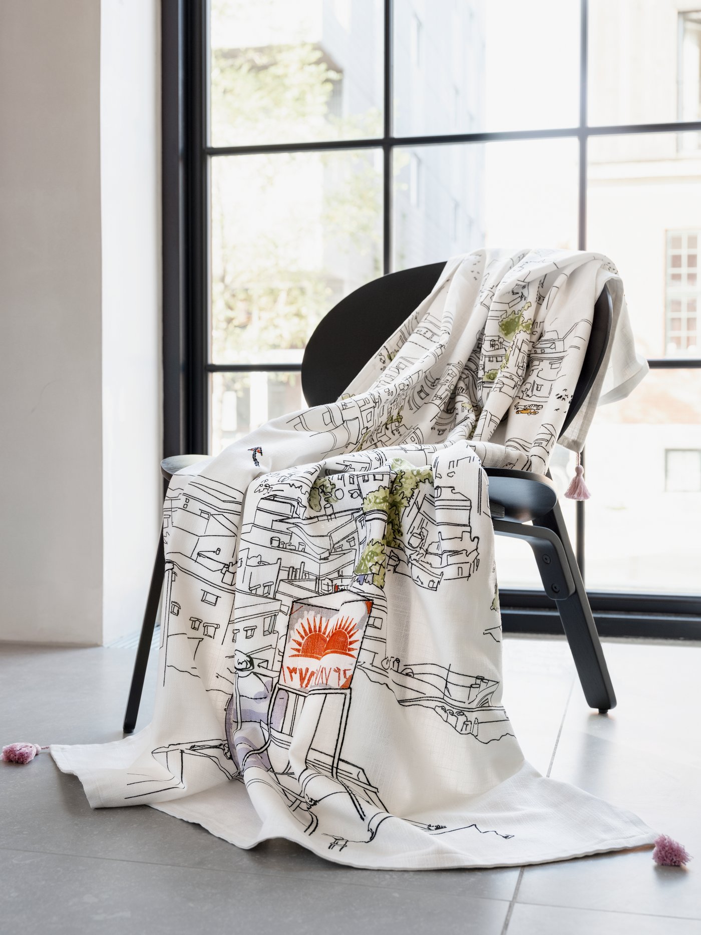 A throw, printed with hand-embroidered details, showing city life in Amman is draped over a chair.