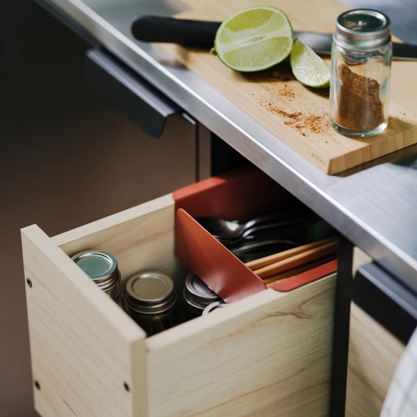 A close-up of a pulled-out ash drawer of an ÄSPINGE kitchenette. There are cutlery and small jars with lids in the drawer.