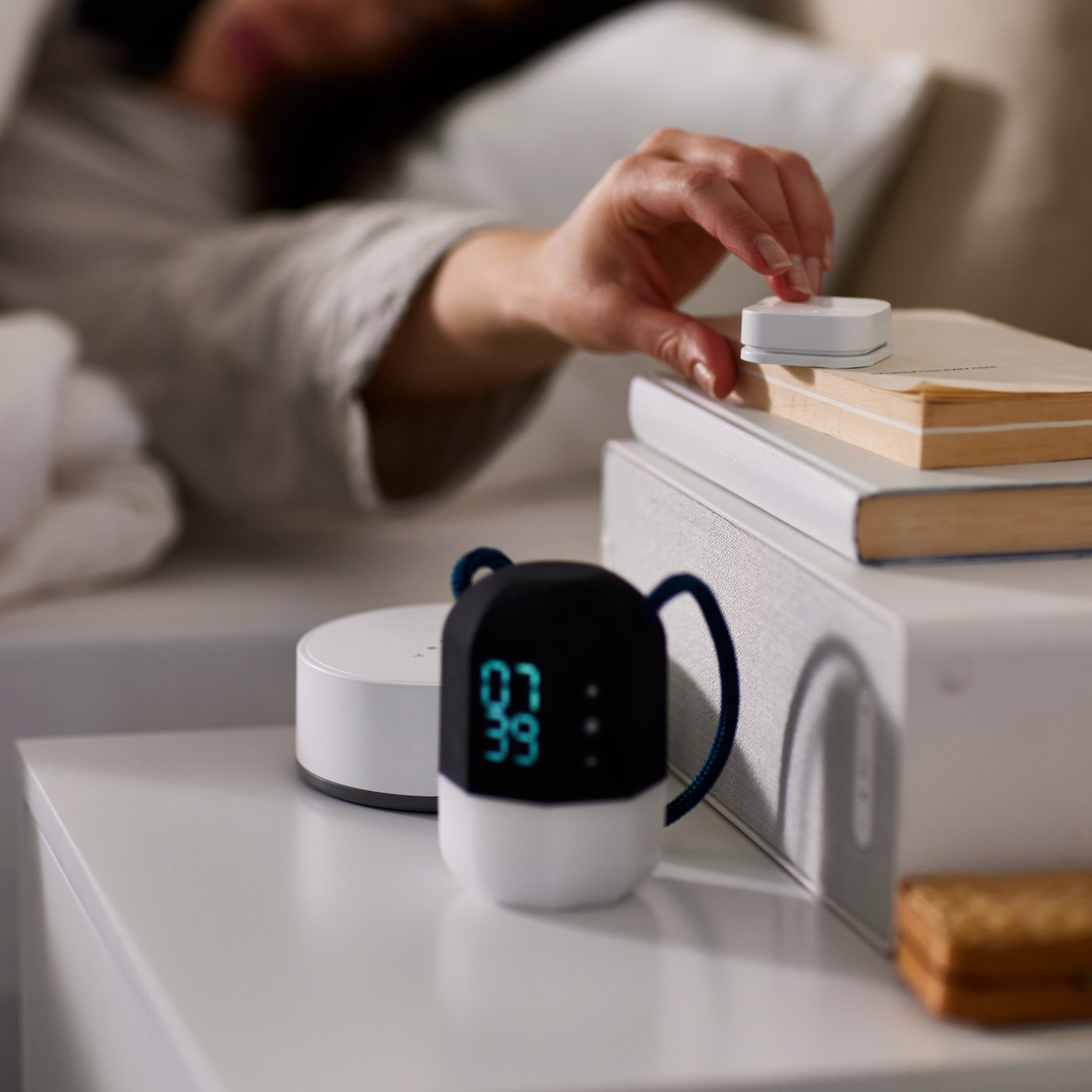 Une femme tend la main pour appuyer sur une commande SANS FIL située au-dessus d'un haut-parleur SYMPHONIQUE sur une table de chevet.