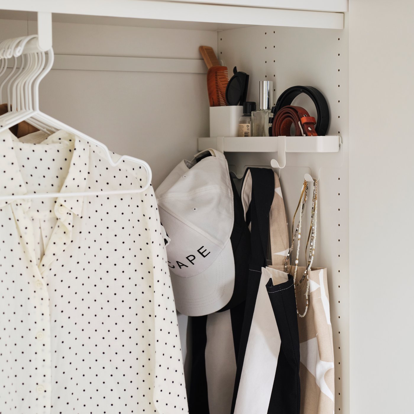 A neatly arranged wardrobe where bags, a cap and small items hang on the ALTARLIDEN hook rack with storage next to clothes.