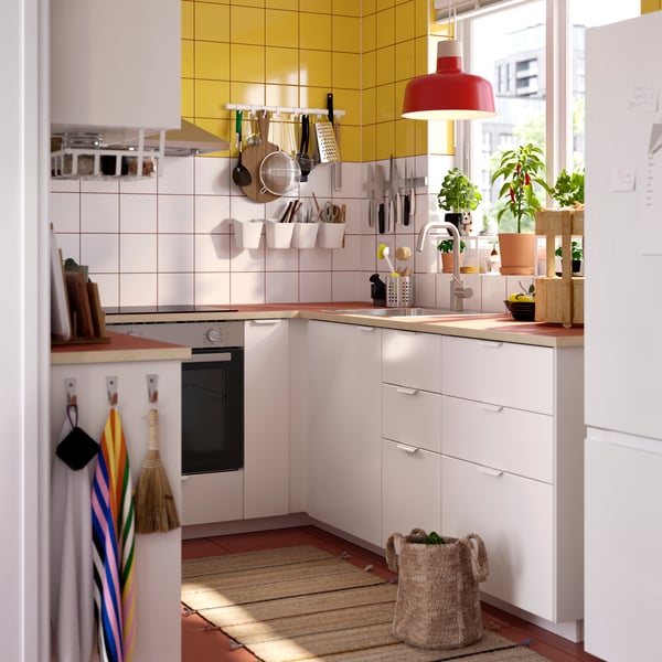 A kitchen with VEDDINGE white drawer fronts and doors, plants in the window, items hanging from the wall and a ceiling lamp.