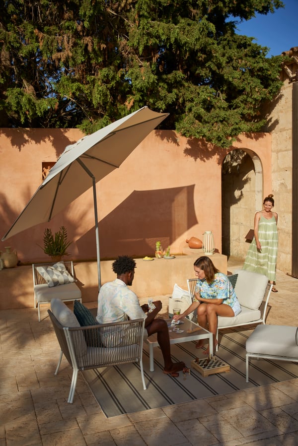 To personer sidder i havemøbler på terassen under en parasol. 
