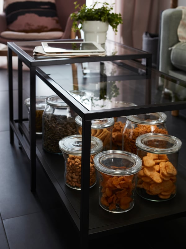 Lidded jars filled with snacks, including IKEA 365+ round glass 1.0 litre jars, on the bottom shelf of a living room table.