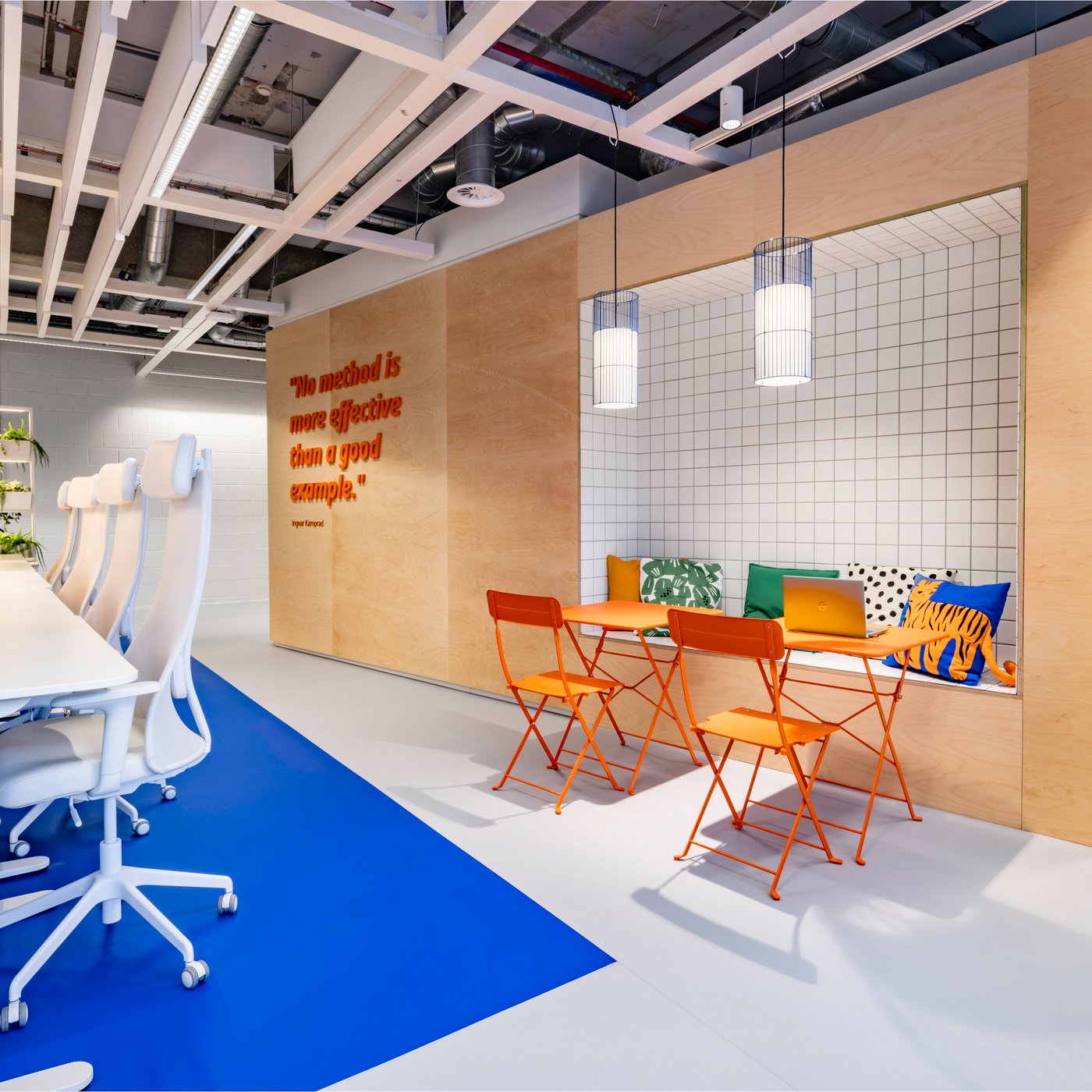 Un espace de travail lumineux avec des assises IKEA confortables et un coin assis délimité avec des chaises de café orange crée une combinaison accueillante entre concentration et discussion informelle.
