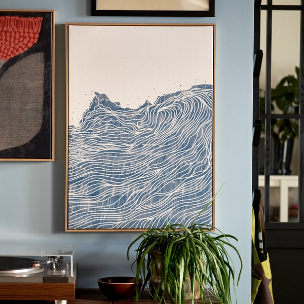 Une section de mur bleu clair où des photos encadrées de la collection BLODFLÄDER sont accrochées côte à côte au-dessus d’une plante en pot feuillue et d’un tourne-disque.